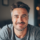 Homme souriant avec une barbe et cheveux gris.