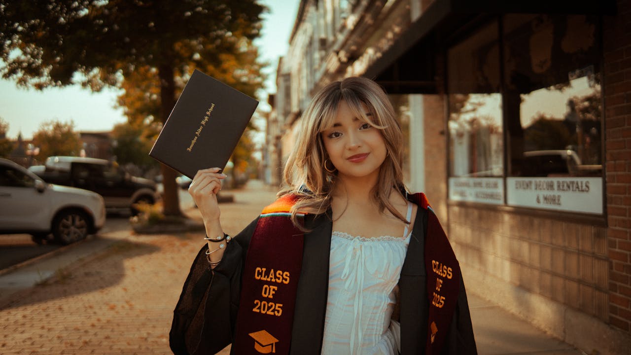 Smiling young graduate holding diploma outdoors, wearing Class of 2025 gown.
